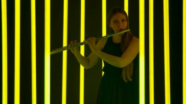 Profesyonel kadın flütçü tarafından seslendirilen klasik müzik senfonisi konseri. Güzel bir kadın flüte melodi üflüyor. Parlak neon ışıkların arka planına karşı siluet. Yavaş çekim.