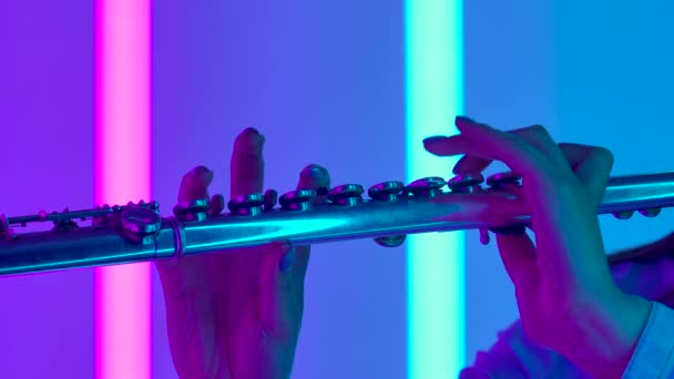 Concerto musicale di musica classica eseguito da una flautista professionista. Mani femminili con un flauto da vicino. Strumento a fiato sullo sfondo di luci al neon luminose. Rallentatore. — Video Stock