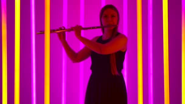 Професійна жінка-музикант грає швидку, веселу мелодію на флейті. Молода жінка грає на вечірці серед яскравих неонових вогнів. Силует. Повільний рух. — стокове відео