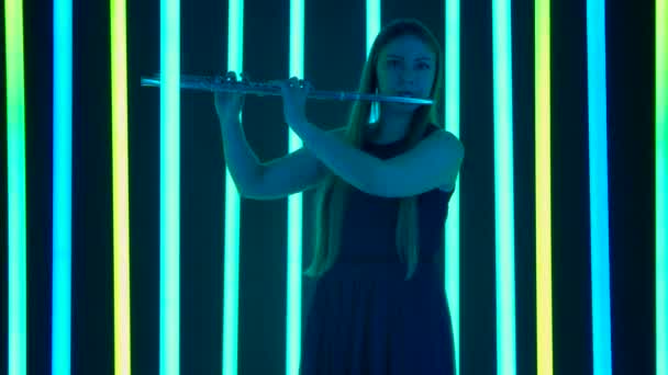 Professionelle Musikerin spielt eine schnelle, lustige Melodie auf einer Flöte. Eine junge Frau tritt auf einer Party unter grellem Neonlicht auf. Silhouette. Zeitlupe. — Stockvideo