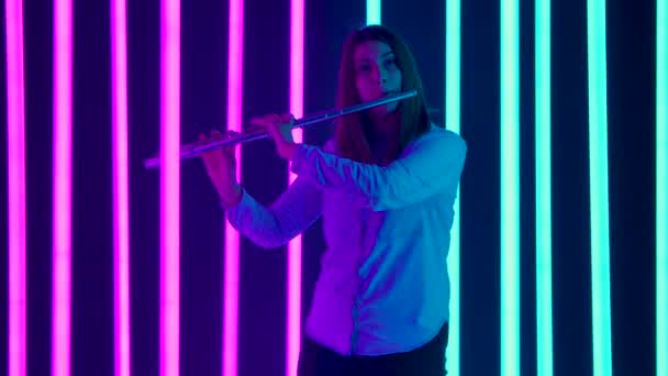 Virtuoso performance of a professional flutist in the musical theater orchestra. A cute woman plays a classical melody on a flute against a background of bright neon lights. Silhouette. Slow motion. — Stock Video