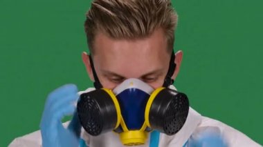 Beyaz koruyucu kıyafetli ve kameraya bakan ameliyat eldivenli bir erkek doktorun portresi tıbbi solunum cihazı ve güvenlik gözlüğü takıyor. Yeşil ekran, krom anahtar. Ağır çekim. Kapat..