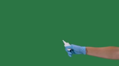 Koruyucu eldivenli erkek eller bir şişe burun ilacını dezenfektan spreyiyle sıkıyor. Coronovirus koruması. Covid 2019 salgınını önlüyor. Yeşil ekran, krom anahtar. Ağır çekim. Kapat..