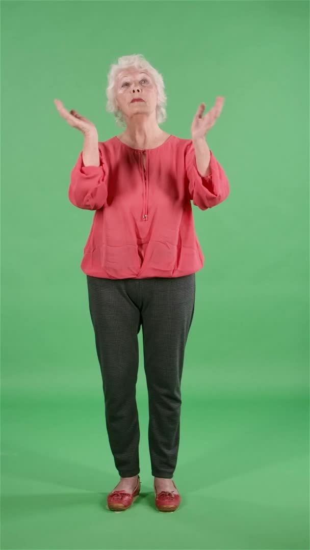 Портрет пожилой женщины, смотрящей в камеру, хлопающей в ладоши от радости и восторга. Серая бабушка в красной блузке на зеленом экране в студии. Медленное движение. Вертикальное видео. — стоковое видео