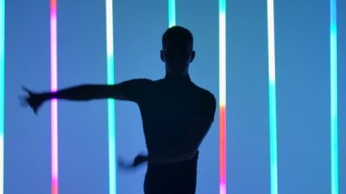 Karanlık bir stüdyoda balo dansçısı solo performansı. Parlak renkli neon tüplerin arka planında siyah bir dansçı silueti. Ağır çekim. Kapat..
