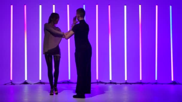 Страстная молодая женщина танцует румбу со своим партнером на ярких разноцветных неоновых лампах. Силуэты красивой пары танцоров движущихся в замедленной съемке. — стоковое видео