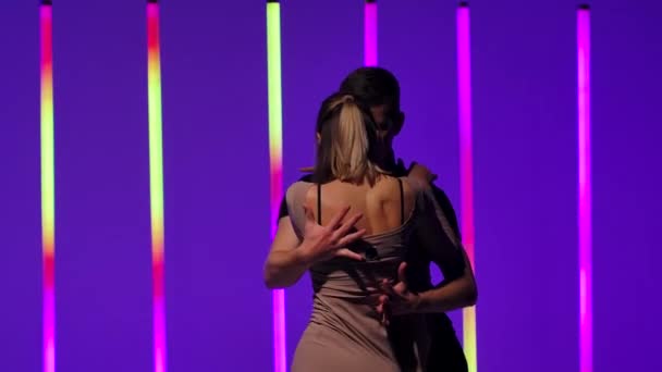 Une paire de danseurs professionnels exécutent des éléments de danse de salon latino-américaine rumba, cha cha cha, samba. Couple dansant dans un studio sombre éclairé par des tubes néons colorés. Au ralenti. Gros plan. — Video