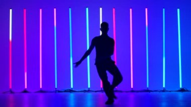 Stüdyoda, parlak renkli neon tüplerin arka planında rumba yapan genç bir adamın karanlık silueti. Adam dansın unsurları üzerinde çalışıyor, adımlar, dönüşler ve zıplıyor. Yavaş çekim.