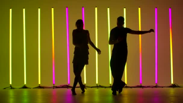 Des danseurs professionnels dansent la rumba en studio sur fond de tubes au néon lumineux. Un mec et une fille s'entraînent aux pas de la danse. Silhouettes sombres de danseurs. Mouvement lent. — Video
