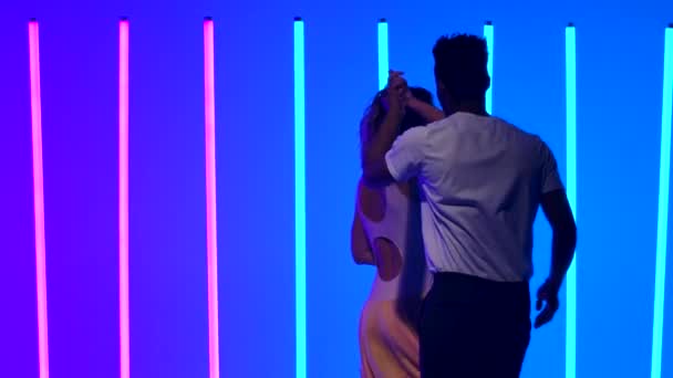 Ballroom dansers oefenen salsa danselementen in de studio tegen een achtergrond van felgekleurde neonlichten. Een zwarte man danst een mooie blanke vrouw. Langzame beweging. Sluiten.. — Stockvideo