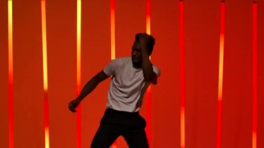Genç siyahi bir adam tarafından sahnelenen salsa dansı. Bir dansçı stüdyoda Latince dans öğelerini ağır çekimde parlak kırmızı turuncu ışıklı arka planda çalışır. Kapat..