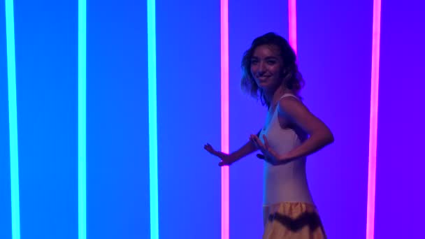 細い踊り手が腰を動かし、サルサダンスの動きを練習する。遅い動きで青とピンクのネオンの背景を背景に、女性がスタジオで踊っている。閉じろ!. — ストック動画