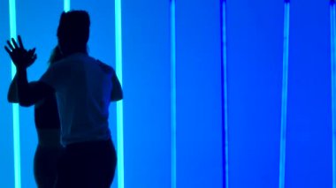 Dansçılar, karanlık bir stüdyoda bir dizi parlak mavi neon ışığa karşı bir dizi dönüş çalışması yapıyorlar. Ağır çekimde salsa yapan bir adamın silueti. Kapat..
