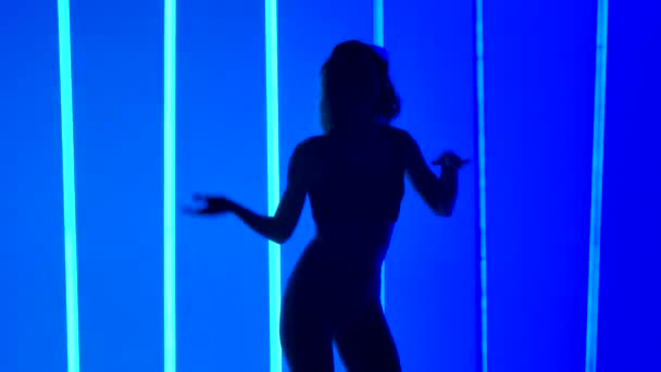 Die schlanke Tänzerin übt die Bewegungen des Salsa-Tanzes, indem sie anmutig ihre Hüften in Zeitlupe bewegt. Silhouette einer Frau im Atelier vor hellblauem Neonlicht. Schließen