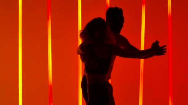 Homme noir et femme caucasienne dansant la salsa passionnément au ralenti. Silhouettes du couple en studio sur fond de tubes néon orange vif et rouge. Gros plan. — Video