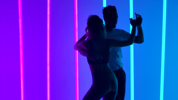 Casal sensual dançando salsa no estúdio contra o pano de fundo de luzes de néon rosa e azul. O conceito de amor, relacionamentos e dança social. Silhuetas. Movimento lento. Fechar. — Vídeo de Stock