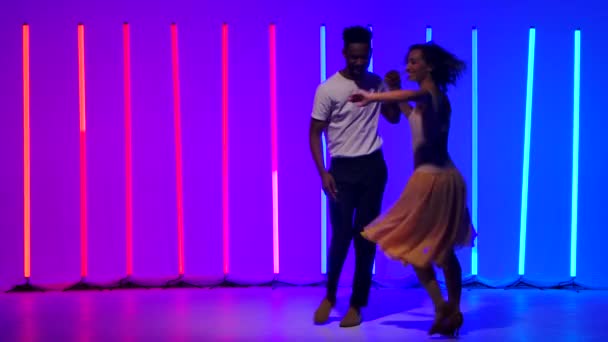 Glücklicher schwarzer Mann und kaukasische Frau üben sich in Streifen und drehen sich im Hintergrund von bunten Neonlichtern. Leidenschaftlicher lateinamerikanischer Salsa-Tanz in Zeitlupe.