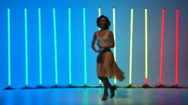 Profesyonel bir balo dansçısından solo performans. Stüdyodaki renkli neon ışıkların arka planında salsa yapan zarif, gülümseyen genç bir kadın. Yavaş çekim.