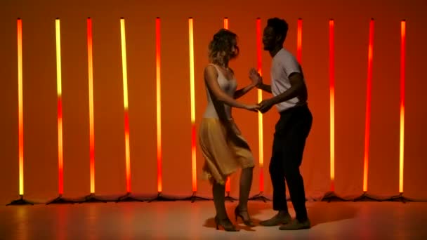 A beautiful sensual couple perform passionate dance steps of Hispanics against a bright red orange neon background. A man and a woman are dancing salsa in slow motion.