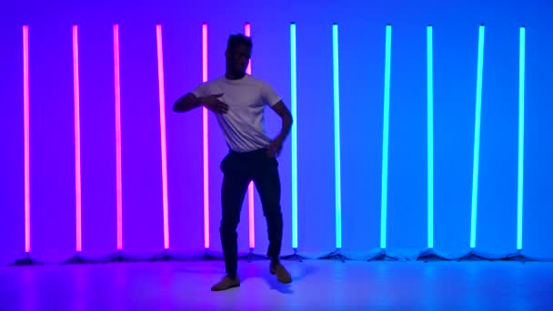 Flexibler afroamerikanischer Mann, der im Studio vor der Kulisse bunter Neonlichter tanzt. Lateinischer Tanz. Salsa. Bachata. Zeitlupe.