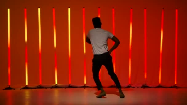 Genç siyahi bir adam tarafından sahnelenen salsa dansı. Bir dansçı stüdyoda Latince dans elementlerini ağır çekimde parlak kırmızı turuncu ışıklı arka planda çalışır.. — Stok video