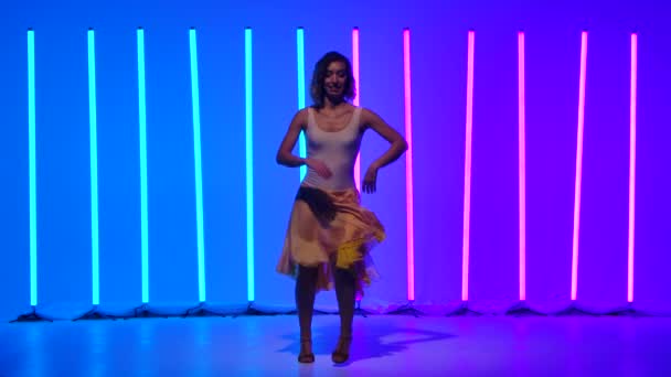細い踊り手が腰を動かし、サルサダンスの動きを練習する。遅い動きで青とピンクのネオンの背景を背景に女性がスタジオで踊っている. — ストック動画