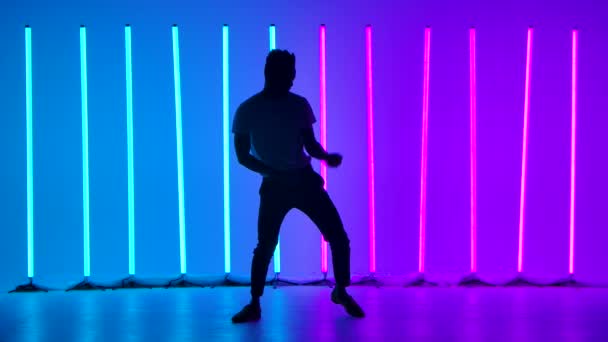 Um dançarino executa um elemento de dança de um programa de salsa em câmera lenta. Silhueta de homens contra o fundo de luzes de néon multicoloridas no estúdio. — Vídeo de Stock