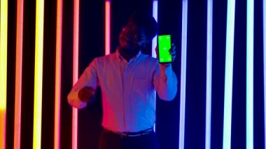 Genç, şık, Afro-Amerikan bir erkeğin portresi gülümseyen ve yeşil ekran krom anahtarı olan akıllı telefonu gösteren ve parmağını ona doğrultan. Yavaş çekim.