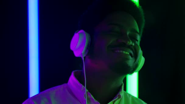 Retrato de um jovem afro-americano elegante vestindo grandes fones de ouvido brancos sorrindo e apreciando a música. Fecha. Movimento lento. — Vídeo de Stock