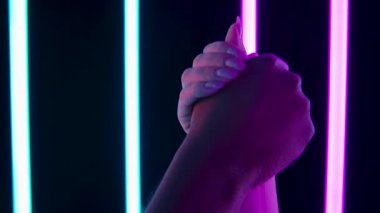 Irkçılık karşıtı sembol. Siyah ve beyaz eller, karanlık bir stüdyodaki parlak neon ışıkların arka planına karşı protesto etmek için bir yumrukta kenetlendi. Kapatın. Yavaş çekim.