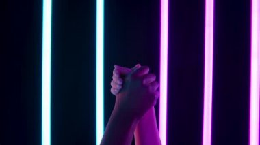 Irkçılık karşıtı sembol. Siyah ve beyaz eller, karanlık bir stüdyodaki parlak neon ışıkların arka planına karşı protesto etmek için bir yumrukta kenetlendi. Kapatın. Yavaş çekim.