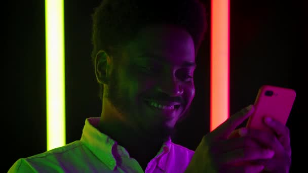 一个年轻时尚的非裔美国男性在智能手机上微笑和发短信的肖像。靠近点慢动作. — 图库视频影像