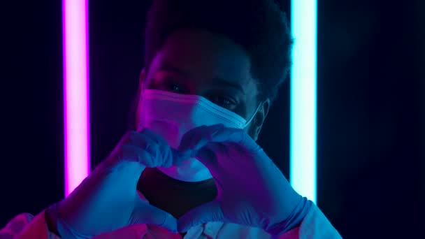 Retrato de um jovem afro-americano elegante em uma máscara médica mostra um gesto para o coração com as mãos em luvas de proteção. Fecha. Movimento lento. — Vídeo de Stock