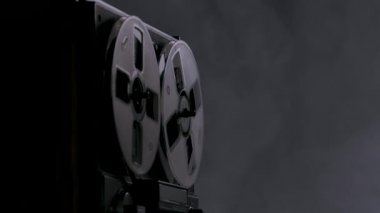 Arka plan dumanlı karanlık stüdyoda arka fonda klasik makaradan makaraya kayıt cihazı. Erkek eli eski siyah kayıt cihazını da içeriyor. Kapatın. Yavaş çekim.