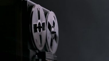 Ses makarası teybe, analog ses depolama cihazı. Kaset, arka plandaki karanlık stüdyoda arka planda müzik çalar. Tek renkli olsun. Dönen makara transparan, yakın plan. Yavaş çekim.