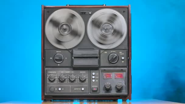 Reel to reel tape recorder playing against a smoky studio background with blue neon lights. Man hand stops playing tape recorder. Rotating vintage music player. Slow motion. — Stock Video