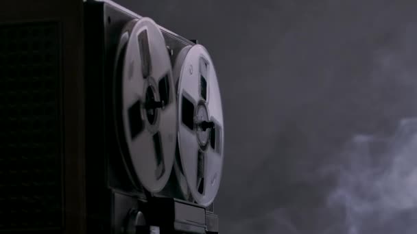 Audio reel to reel tape recorder, analog audio storage device. Tape deck plays music on dark background smoky studio with backlight. Monochrome. Spinning reels transparent close up. Slow motion. — Stock Video