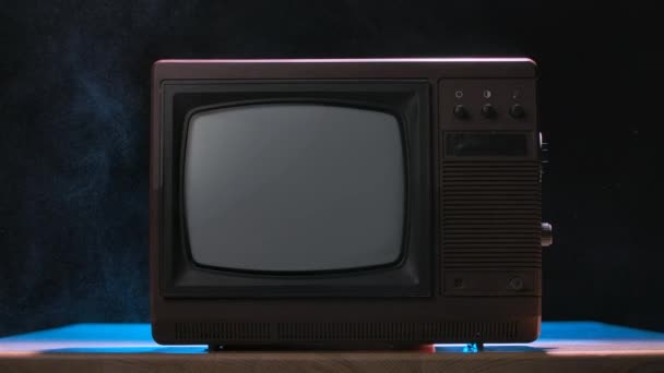 Muž zapne starou retro televizi a odfoukne prach. Ročník televize na zakouřeném pozadí studia s modrými neonovými světly. Mužské ruce zblízka. Zpomalený pohyb. — Stock video