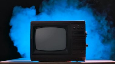 Düğmeli eski tarz TV seti. Eski moda TV, dumanlı bir stüdyonun arka planına karşı mavi neon ışıklar ve toz parçacıkları. Yavaş çekim.