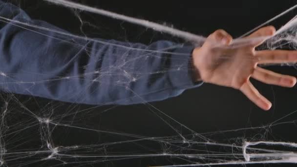 A man hand tears apart a terrible white web. Decorations for the celebration of Halloween night on a black studio background. Close up. Slow motion. — Stock Video