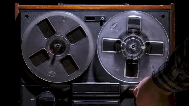 Pria tangan menjalankan gulungan antik untuk reel tape recorder terhadap latar belakang studio hitam. Pemutar musik analog dalam gelap. Tampilan depan menutup. Tren disko populer 70-an, 80-an. Gerakan lambat. — Stok Video