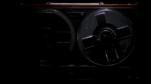 From the darkness looms vintage reel to reel tape recorder against a black studio background. Retro analogue music player. Front view close up. Popular disco trends 70s, 80s. Slow motion. — Stock Video