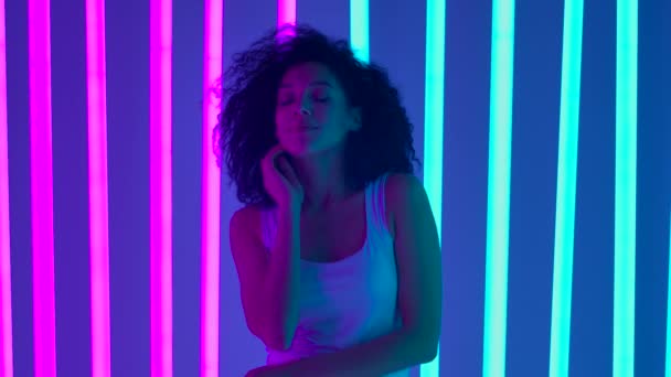 Portret van een jonge leuke Afro-Amerikaanse vrouw die flirt en koket poseert voor de camera. Een meisje in een donkere studio met felgekleurde neonlichten. Langzame beweging. Sluiten.. — Stockvideo