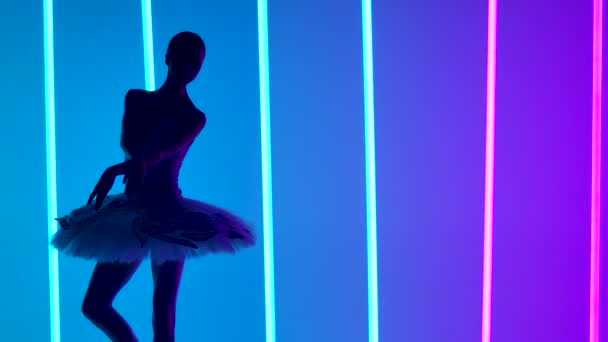 Femminile giovane ballerina graziosa danza elementi di balletto classico in uno studio buio su uno sfondo di luci al neon blu e viola. Silhouette sottile. Chiudete. Rallentatore. — Video Stock