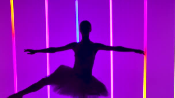 Витончена балерина танцює частину білого лебедя, виконуючи піруети. Силует красивої стрункої фігури на тлі яскравих неонових вогнів у темній студії. Повільний рух. крупним планом . — стокове відео