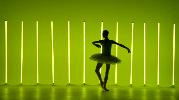 A rugalmas fiatal balerina klasszikus lépésekkel próbálja ki a fehér hattyú egy részét. Silhouette egy karcsú női táncos hátterében fényes neon fények sötét stúdióban. Lassú mozgás.. — Stock videók