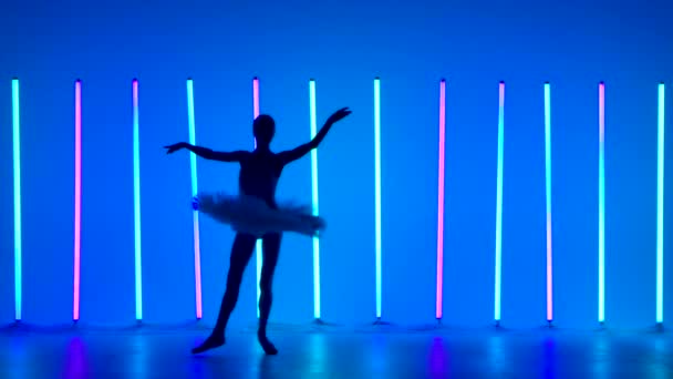 Klasik bale koreografisi. Genç balerin dans adımları atar ve karanlık bir stüdyoda parlak neon ışıkların arkasına atlar. Beyaz etekli siluet kadın dansçılar. Yavaş çekim. — Stok video