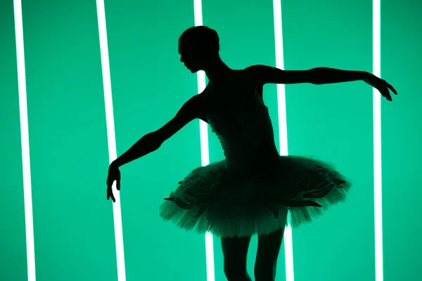 Krásná mladá baletka tančící klasický balet v tmavém studiu na pozadí jasných neonových světel. Silueta štíhlé tanečnice v bílé sukni a špičatých botách. — Stock fotografie