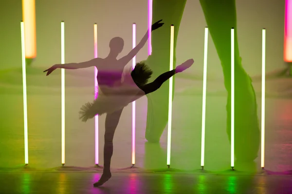 Koláž stínů baletky mladé ženy, která tančí a pózuje v tmavém studiu s jasnými neonovými světly. Silueta štíhlého modelu v bílé sukni a špičatých botách. Plakát baletní školy. — Stock fotografie