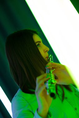Flüt çalan genç ve güzel bir müzisyenin yan görünümü. Kadın flütçü, karanlık bir stüdyoda parlak neon ışıklarının arka planına karşı rüzgar enstrümanı çalıyor. Kapat..